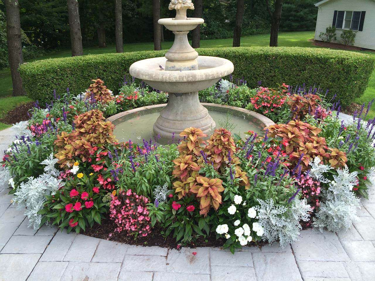 A Water Fountain Surrounded By Flowers 