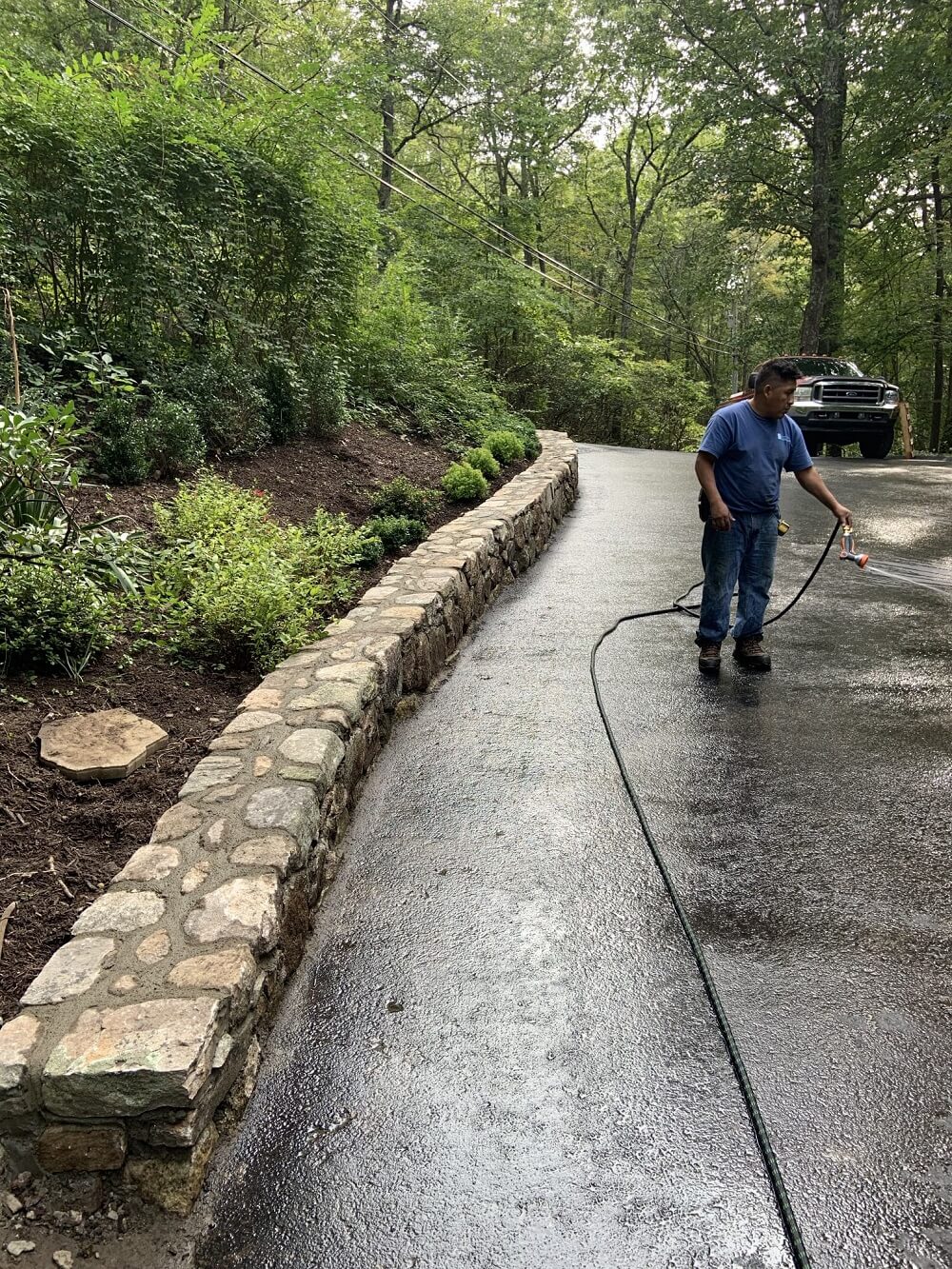 A man performing landscape maintenance by cleaning a driveway with a hose.